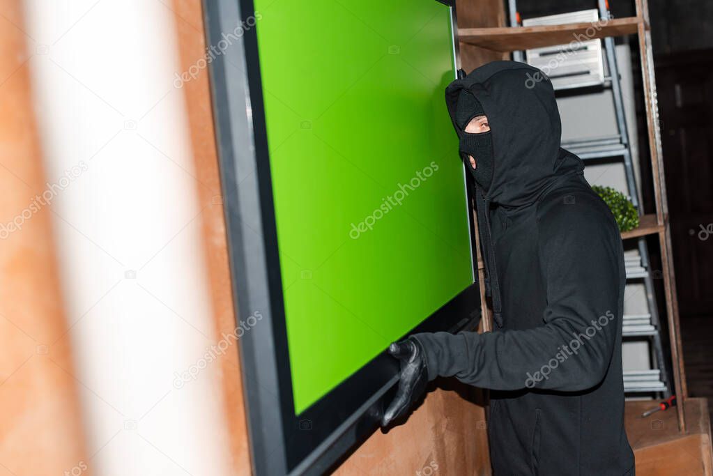 Selective focus of robber in mask holding tv during stealing