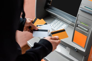 Cropped view of burglar holding credit cards near atm  clipart