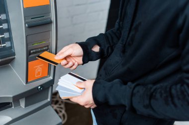 Cropped view of thief holding credit cards near automated teller machine clipart