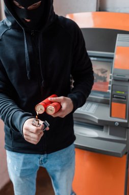 Robber in balaclava holding dynamite and lighter near automated teller machine clipart