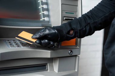 Cropped view of burglar in leather glove holding credit card near atm  clipart