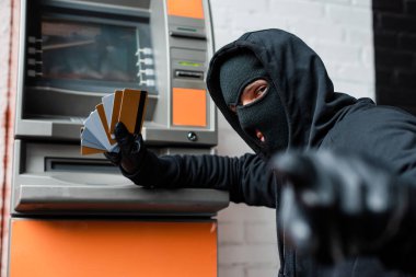 Kar maskeli hırsızın seçici odağı ATM 'nin yanında kredi kartı tutarken kamerayı işaret ediyor. 