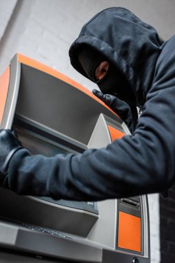 Low angle view of burglar in balaclava and lather gloves holding automated teller machine clipart