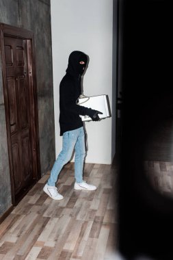 Side view of robber holding microwave oven while walking near house door  clipart