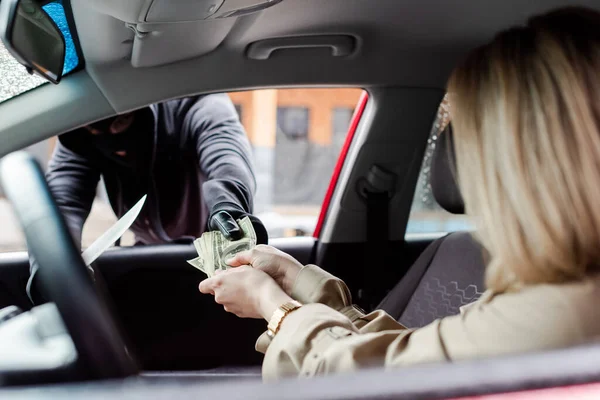 妇女向汽车附近持刀抢劫犯提供现金的选择性焦点 — 图库照片