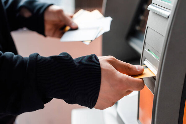 Cropped view of thief holding credit cards while using automated teller machine