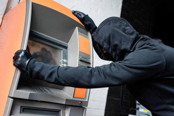 Side view of burglar in mask and leather gloves holding atm 