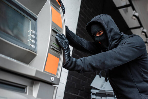 Selective focus of burglar in mask pulling atm 