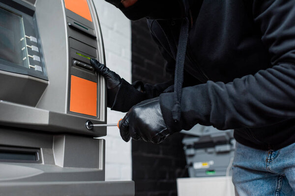 Обрезанный вид грабителя в кожаных перчатках с отверткой рядом с банкоматом
 