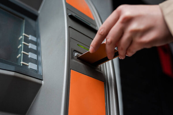 Cropped view of woman holding credit card while using atm 