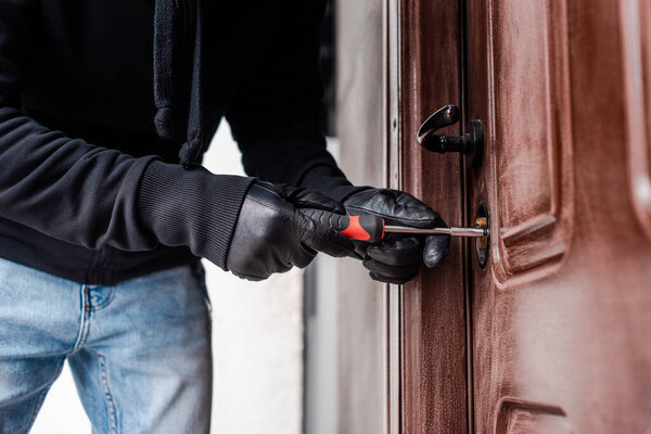 Cropped view of housebreaker in leather gloves breaking door lock with screwdriver 