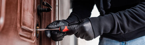 Panoramic orientation of robber in leather gloves opening door lock with screwdriver 