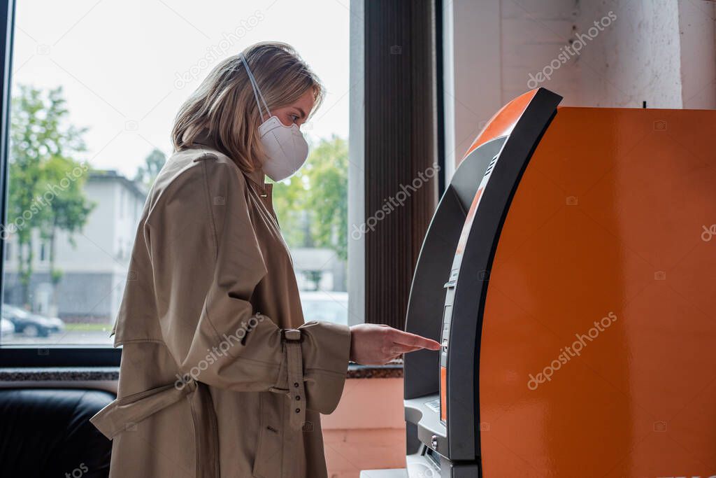 Side view of woman in medical mask using atm 