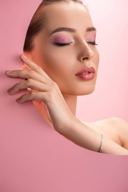 beautiful naked woman with shiny makeup in round paper hole with closed eyes isolated on pink clipart