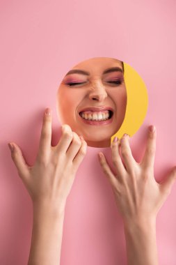 Pembe kağıt delikte parlak makyajlı güzel bir kadının portresi sarı üzerinde izole edilmiş dişleri gösteriyor.