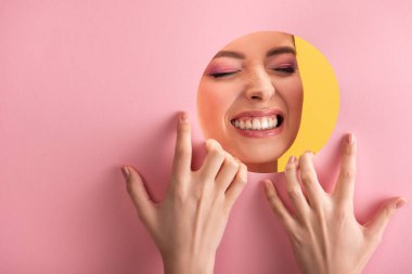 Pembe kağıt delikte parlak makyajlı güzel bir kadının portresi sarı üzerinde izole edilmiş dişleri gösteriyor.