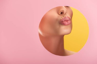Pembe kağıt delikte parlak dudakları olan güzel bir kadının kısmi görüntüsü. Sarı renkte izole edilmiş dudakları somurtuyor.