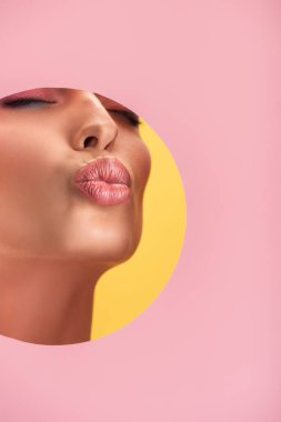 Pembe kağıt delikte parlak dudakları olan güzel bir kadının kısmi görüntüsü. Sarı renkte izole edilmiş dudakları somurtuyor.