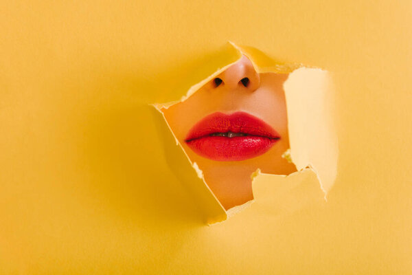 cropped view of beautiful woman with crimson lips in yellow paper torn hole