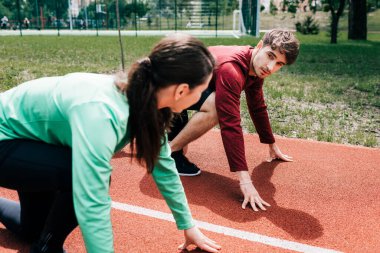 Erkeğin açık havada koşu parkurunda başlangıç pozisyonunda dururken kadına bakışının seçici odağı 