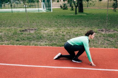 Parktaki koşu yolunda başlangıç pozisyonundaki sporcunun yan görünümü 