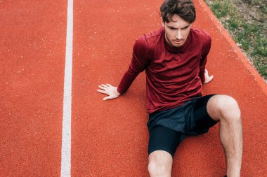 Parkta koşu pistinde oturan yakışıklı sporcunun yüksek açılı görüntüsü 