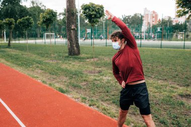 Tıp maskeli sporcu parkta spor yapıyor. 