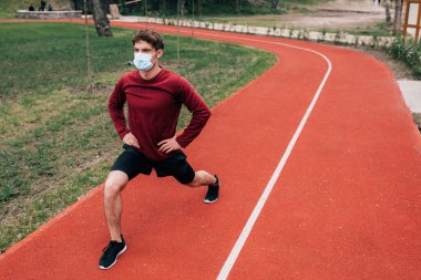 Sağlık maskeli sporcu parkta koşarken hamleler yapıyor. 