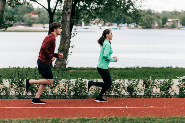 Side view of couple running on running track in park 