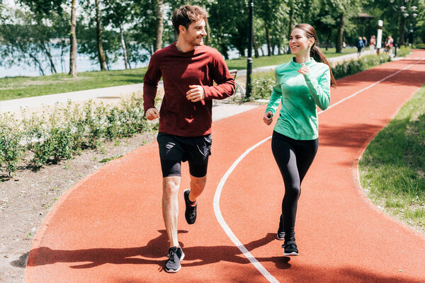 Sportswoman smiling at boyfriend while running on track in park 