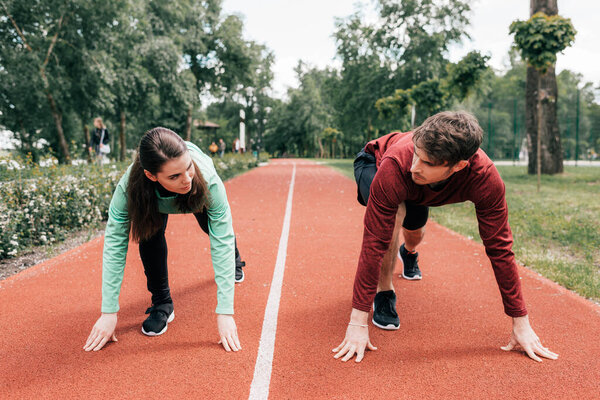 Couple looking at each other while standing in starting position on running track in park 