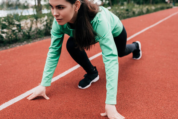 Attractive woman standing in starting position on running track while training in park 