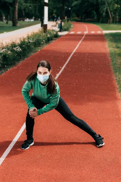 戴着医疗面罩的女运动员在公园的跑道上跑步 — 图库照片
