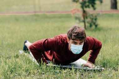 Medikal maskeli sporcunun seçici odak noktası parktaki spor minderinde şınav çekiyor. 