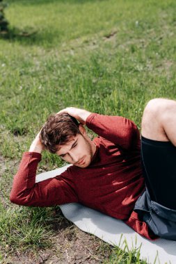 Yakışıklı sporcunun seçici odak noktası parktaki spor minderinde karın kası yapması. 