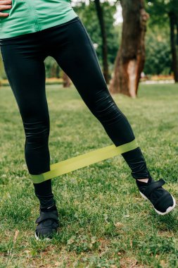 Parkta antrenman yaparken direniş bandı kullanan sporcu kadın görüntüsü 
