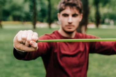 Parkta antrenman yaparken elastik bant kullanan sporcunun seçici odak noktası 