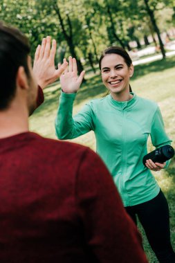 Parkta spor şişesini tutarken adama beşlik çakmanın seçici odak noktası. 