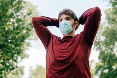 Sağlık maskeli sporcunun arka planda mavi gökyüzü ile parkta yaptığı eğitimin düşük açılı görüntüsü 