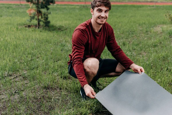 Smuk Sportsmand Ser Kameraet Mens Holder Fitness Mat Nær Græs - Stock-foto