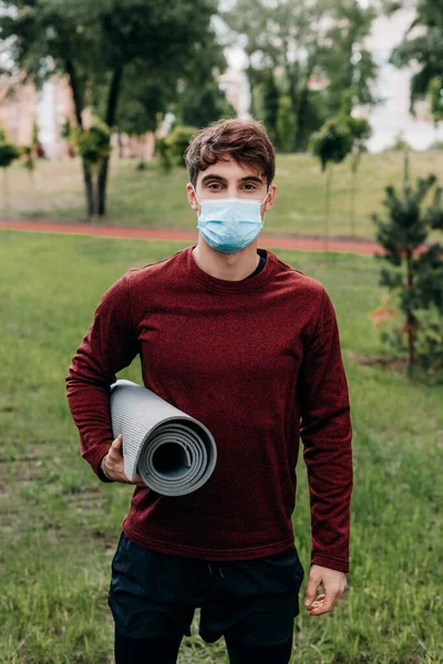 Jovem Desportista Máscara Médica Olhando Para Câmera Enquanto Segurando Tapete — Fotografia de Stock