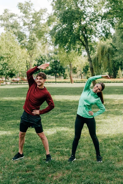 Joven Pareja Sonriente Haciendo Ejercicio Césped Cubierto Hierba Parque — Foto de Stock