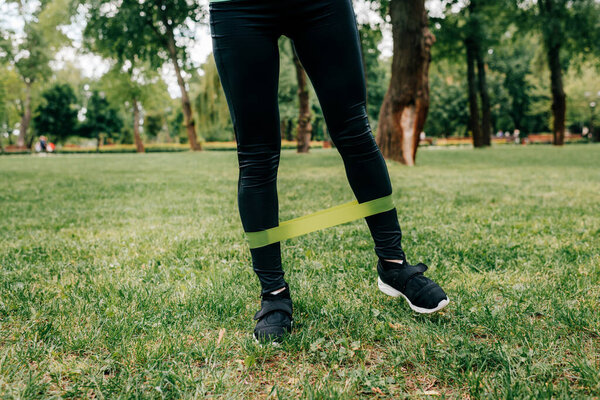 Cropped view of sportswoman exercising with resistance band in park 