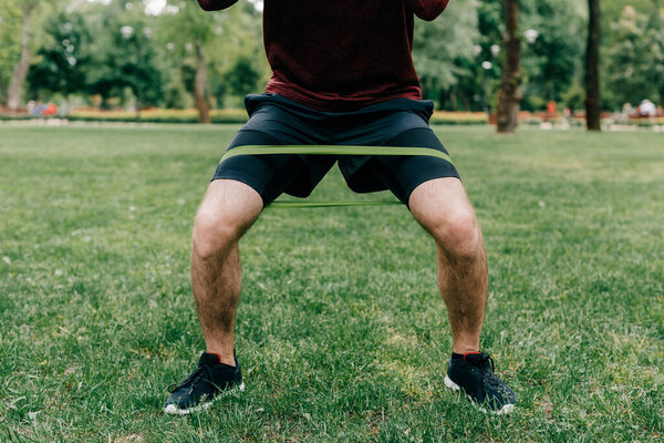 Cropped view of young sportsman using resistance band while working out in park 