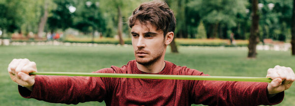 Panoramic crop of sportsman pulling up resistance band in park 