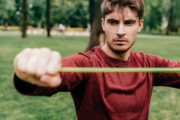 Selective focus of handsome man exercising with resistance band in park 