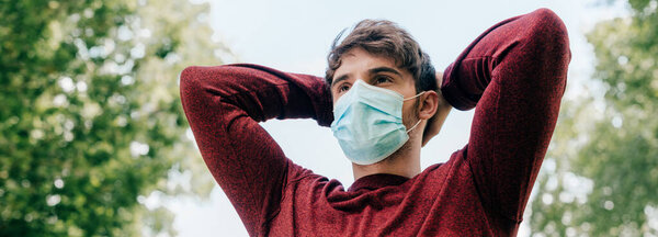 Panoramic crop of sportsman in medical mask training in park with sky at background 
