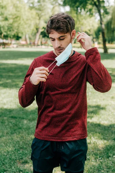 Bonito Jovem Desportista Segurando Máscara Médica Parque — Fotografia de Stock