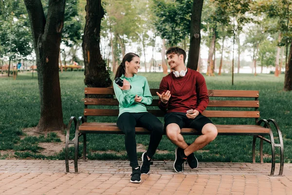 Kulaklıklı Gülümseyen Sporcu Parkta Bankta Duran Kız Arkadaşına Bakıyor — Stok fotoğraf