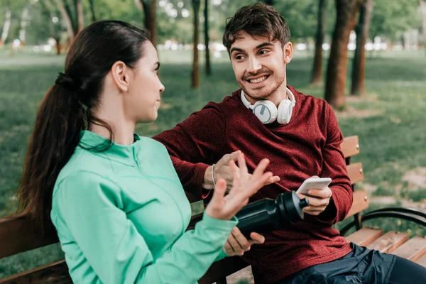 Selektivní Zaměření Usměvavý Sportovec Sluchátkách Držící Smartphone Při Rozhovoru Přítelkyní — Stock fotografie